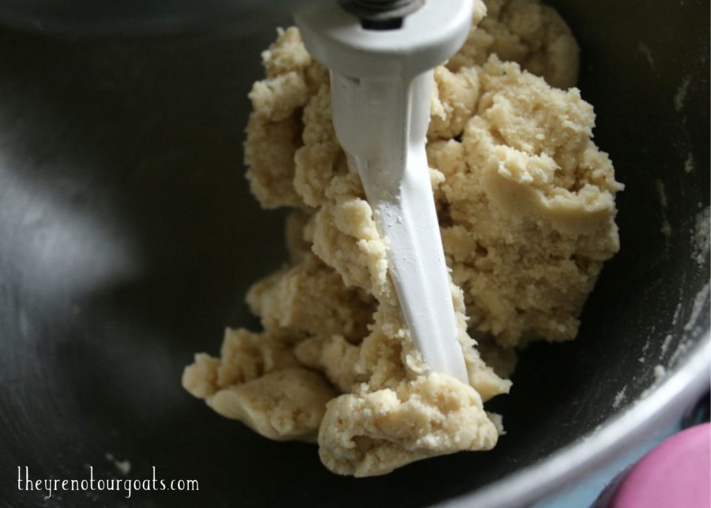 A slightly sticky ball of cookie dough clumped onto the paddle attachment of a stand mixer.